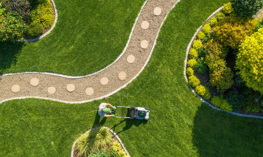 overhead image of man mowing lawn between borders and a curving path